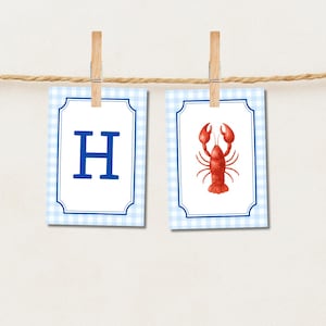 May include: Two rectangular cards with blue gingham borders are clipped to a string. One card displays the letter "H" in blue, the other a red lobster illustration. The cards are white with a blue border and are clipped with wooden pegs.