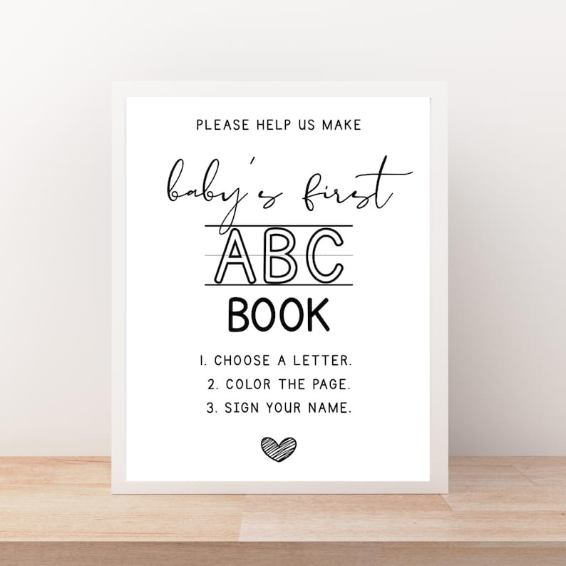 May include: A framed sign with the text "PLEASE HELP US MAKE baby's first ABC BOOK". Instructions include choosing a letter, coloring the page, and signing your name. A heart graphic is at the bottom. The sign is white with black text.