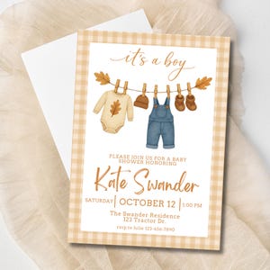 Puede incluir: Invitación a un baby shower con borde de cuadros vichy. La invitación presenta ilustraciones en acuarela de ropa de bebé colgada en un tendedero, con el texto "it's a boy". La invitación incluye el nombre "Kate Swander" y los detalles del evento.