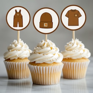 May include: Three cupcakes with white frosting and silver sprinkles. Each cupcake has a circular topper with a brown outline. The toppers feature illustrations of workwear: overalls, a beanie, and a t-shirt.