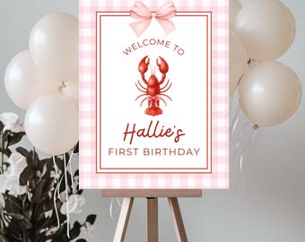 May include: A pink and white gingham sign on an easel, with the text "Welcome to Hallie's First Birthday." A red lobster illustration is centered on the sign, with a pink bow at the top. White balloons and flowers are in the background.