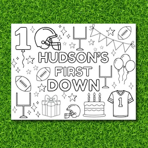 May include: A black and white coloring page with a football theme. The text "HUDSON'S FIRST DOWN" is displayed, along with footballs, helmets, a jersey, a cake, and other celebratory graphics. The number 1 is featured with a balloon.