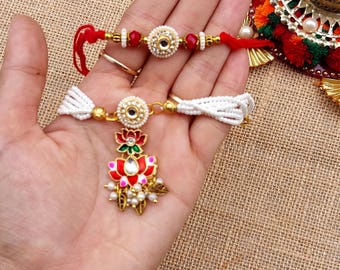 May include: Two ornate, gold-toned bracelets with red and white accents. One features a central floral design with red, green, and white details, and small pearls. The other has a central circular design with a central stone and red beads. Both are on a tan background.