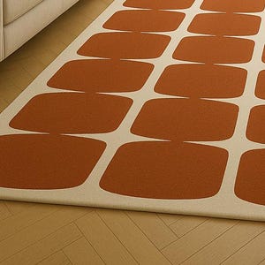 May include: A rectangular rug featuring a repeating pattern of rust-coloured, rounded rectangles against a cream background. The rug is placed on a wooden floor, with a glimpse of a cabinet in the upper left corner.
