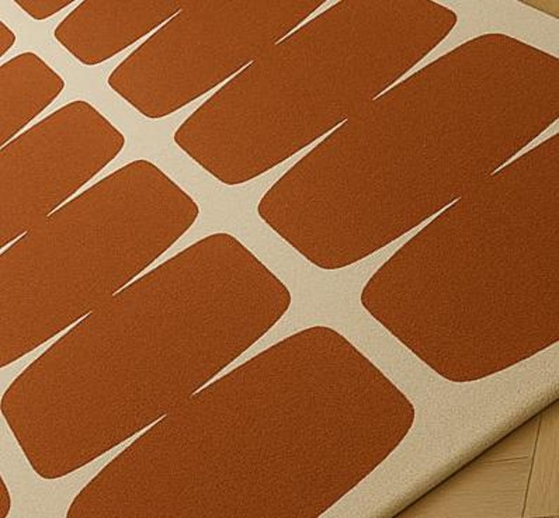 May include: A close-up of a rug featuring a repeating pattern of rust-coloured rectangular shapes with white, pointed extensions. The rug has a soft, textured appearance, and the design is modern and geometric.