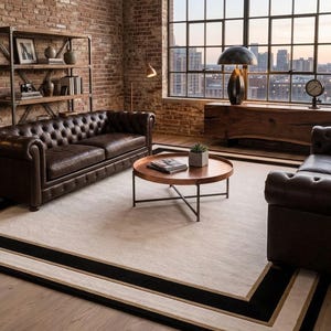 Puede incluir: Una alfombra rectangular con un gran centro de color crema bordeado por una franja negra gruesa y un marco exterior de color tostado m&aacute;s fino. La alfombra est&aacute; colocada sobre un suelo de madera clara en una habitaci&oacute;n con sof&aacute;s de cuero.