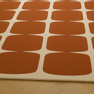May include: A rectangular rug featuring a repeating pattern of rust-coloured, rounded rectangles on a cream background. The rug is made of a soft material, suitable for a living room or bedroom.