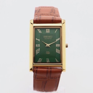 Peut inclure: Une montre-bracelet rectangulaire Seiko Quartz avec un boîtier doré, un cadran vert profond orné de chiffres romains dorés et un bracelet en cuir marron à motif crocodile texturé avec une boucle ardillon de couleur dorée.