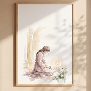 May include: Watercolor art print in a wooden frame. The artwork depicts a person kneeling in prayer, wearing a pink robe, with a candle and flowers. The background features architectural elements in soft, warm tones. The print is displayed above a wooden bench.