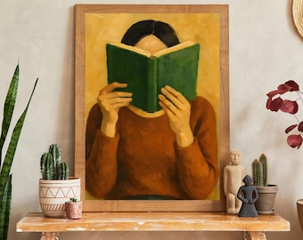 Peut inclure: Peinture à l'huile encadrée représentant une personne lisant un livre vert, vêtue d'un pull marron. Le fond est jaune. Le tableau est posé sur une table en bois avec des plantes et des figurines.