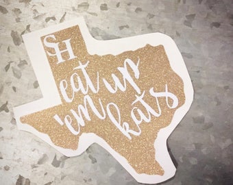 May include: A gold glitter Texas-shaped sticker with the text "Sh eat up 'em kats" in white lettering.