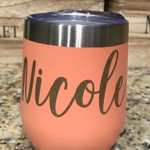 May include: A peach-colored stainless steel tumbler with a silver lid. The tumbler has the name "Nicole" written in gold glitter lettering.