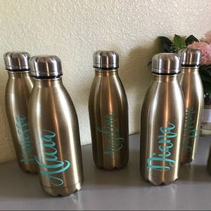 May include: Five gold-colored water bottles with personalized names in teal lettering. The names are "Melissa", "Alicia", "Angelina", "Diana", and "Jasmine".