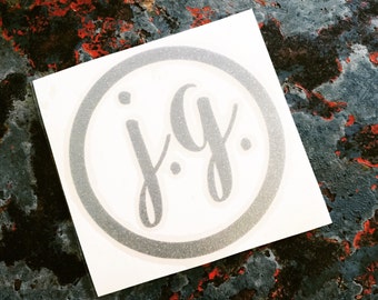 May include: A white sticker with a silver glitter circle and the text "j.g." in a silver glitter font.