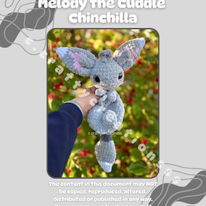 Pu&ograve; includere: Un peluche di cincill&agrave; all'uncinetto nei toni del grigio, blu e rosa. Il giocattolo ha grandi orecchie, un corpo soffice e una piccola coda. Il testo "Melody the Cuddle Chinchilla" &egrave; nella parte superiore dell'immagine.