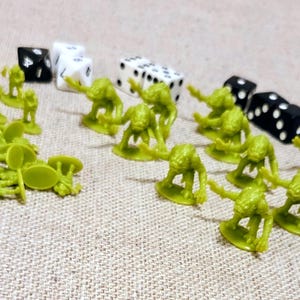 May include: A collection of green plastic game pieces, including miniature figures and dice. The dice are black and white with white dots. The figures are in various poses, suggesting a tabletop game.
