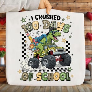 Puede incluir: Bolso de mano blanco con un dinosaurio de dibujos animados conduciendo un monster truck. El texto dice "I Crushed 100 Days of School." El dinosaurio lleva gafas de sol y una mochila.