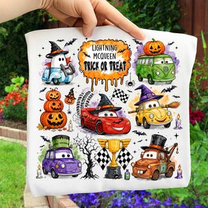 May include: A white t-shirt featuring a colorful Halloween-themed graphic with cartoon cars dressed in costumes, including a red race car, a yellow car with a witch hat, and a purple car, alongside pumpkins, a trophy, and the text Lightning McQueen Trick or Treat.