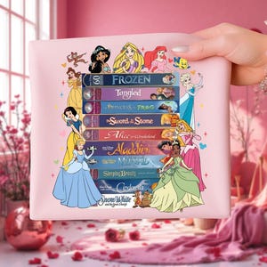 Puede incluir: Un bolso tote rosa con ilustraciones de princesas de Disney y títulos de películas como "Frozen", "Tangled" y "Cinderella". El bolso tiene una pila de cintas VHS con los títulos de las películas. Las princesas están dibujadas en un estilo de dibujos animados.
