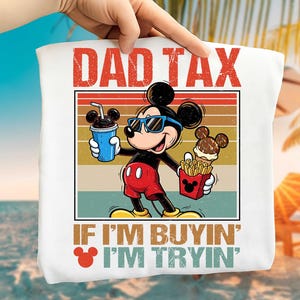 May include: White tote bag featuring Mickey Mouse wearing sunglasses and holding a drink and fries. The text "DAD TAX" is at the top, with "IF I'M BUYIN' I'M TRYIN'" at the bottom.