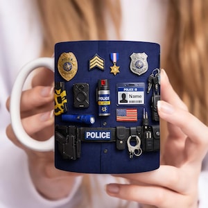 May include: A white ceramic mug featuring a design of police uniform elements. The design includes a badge, stripes, a medal, a detective badge, a body camera, OC spray, a police ID, an American flag, and handcuffs.