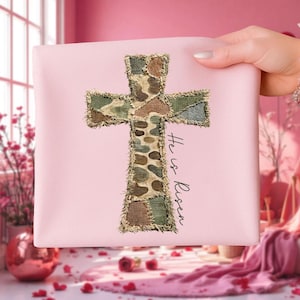 Peut inclure: Un carré rose avec un motif de croix. La croix est faite de tissu patchwork dans des tons de vert, marron et beige. Le texte "He is Risen" est écrit en police script sur le côté droit de la croix.