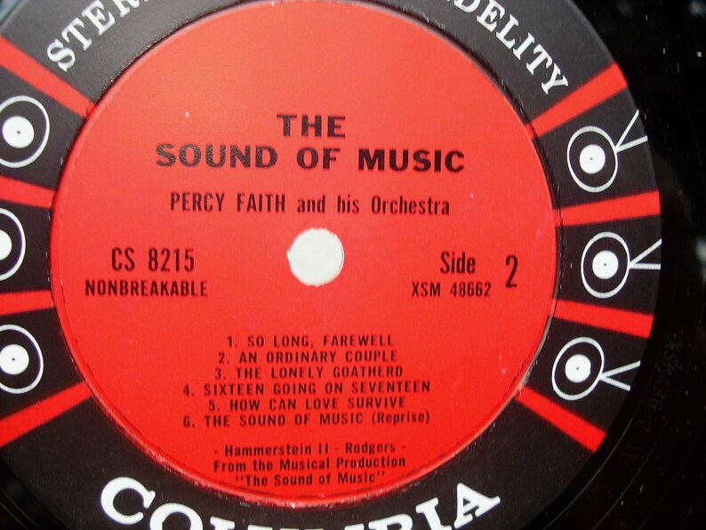 May include: A vintage vinyl record for "The Sound of Music" by Percy Faith and his Orchestra. The red label features black and white text, including song titles and "Side 2." The record is labelled "Nonbreakable."