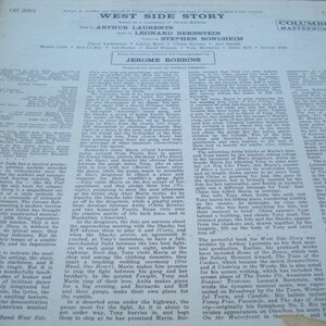 May include: A black and white photograph of a record album cover for the musical West Side Story. The cover features the title of the musical in white text on a black background. The names of the actors, writers, and composers are listed below the title. The Columbia Masterworks logo is in the top right corner.
