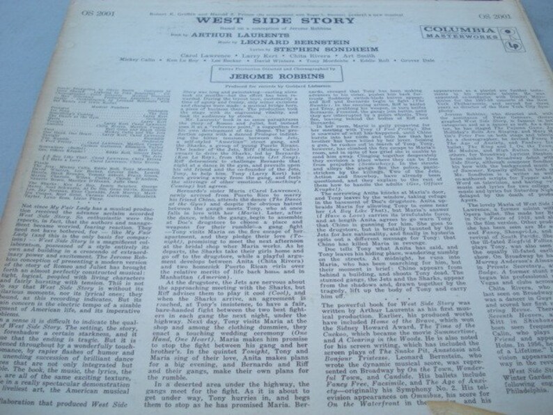 May include: A black and white photograph of a record album cover for the musical West Side Story. The cover features the title of the musical in white text on a black background. The names of the actors, writers, and composers are listed below the title. The Columbia Masterworks logo is in the top right corner.