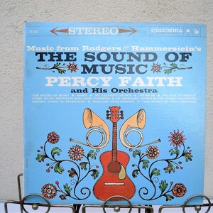 May include: A vintage vinyl record album cover for "The Sound of Music" by Percy Faith and His Orchestra. The album cover is light blue with the title in large white letters. A guitar and horns are featured in the center, with floral accents.