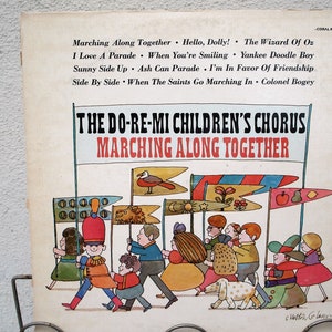 May include: Vintage vinyl record cover for "The Do-Re-Mi Children's Chorus - Marching Along Together." The cover features a colorful illustration of children marching with flags. Song titles are listed at the top, including "Hello, Dolly!" and "Yankee Doodle Boy."