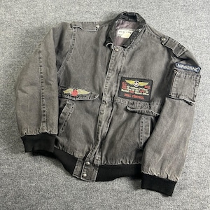 May include: A grey bomber jacket with black ribbed cuffs and hem. The jacket features patches with text and winged emblems, including an "AIRBORNE" patch. The jacket has a black collar and a button-up front.