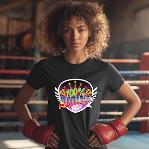 Könnte beinhalten: Schwarzes T-Shirt mit einem farbenfrohen Aufdruck mit der Aufschrift "100% Authentic". Die Grafik hat die Form eines Schildes mit Sternen und Flügeln. Die Person im Bild trägt rote Boxhandschuhe.