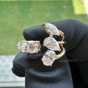 May include: A gold ring with three round diamonds and a second ring with three pear-shaped diamonds. The rings are set against a black background, with the brand name "JewellNYC" visible.