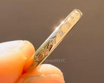 May include: A gold ring with a delicate design, featuring small, sparkling stones. The ring is held between fingers, showcasing its intricate details and elegant style. The ring's surface is adorned with a pattern of small diamonds.