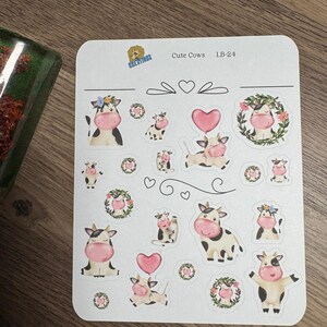 May include: A sheet of stickers featuring various cute cow illustrations. The cows are depicted in black and white with pink noses and accents, some wearing floral crowns or holding heart-shaped balloons. The text "Cute Cows" and "LB-24" are printed on the sheet.