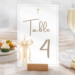 Op de afbeelding: Een tafelnummerkaart met een kaarsillustratie en het woord "Tafel" en het nummer "4". De kaart wordt in een houten voet gehouden. Een glas champagne en hapjes staan op de achtergrond.