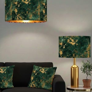 May include: A pair of lamps and cushions with a dark green and gold pattern. The lampshade is cylindrical. The table lamp has a gold base. The cushions are on a black sofa. The lamps are a decorative home item.