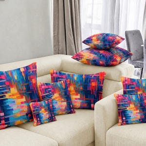 May include: A collection of decorative throw pillows with a vibrant abstract design. The pillows feature a colorful pattern of blue, orange, pink, and yellow rectangles and lines. The pillows are arranged on a cream-colored sofa, creating a modern aesthetic.