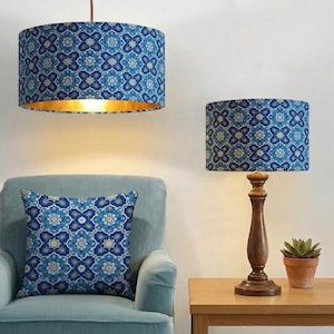 Könnte beinhalten: Ein blau-gold gemusterter Lampenschirm hängt von der Decke, mit einem passenden Lampenschirm auf einer hölzernen Tischlampe. Ein gemustertes Kissen liegt auf einem blauen Sessel. Die Lampenschirme und das Kissen weisen ein sich wiederholendes Blumenmuster auf.