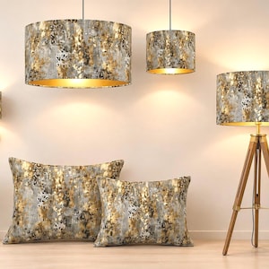 May include: A collection of home decor items featuring a metallic gold, grey, and white abstract pattern. Included are two pendant lights, a wall sconce, a tripod floor lamp, and two rectangular throw pillows, all sharing the same textured design.