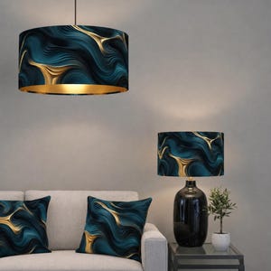 Op de afbeelding: Een hanglamp en een tafellamp met bijpassende lampenkappen, samen met twee sierkussens. De lampenkappen en kussens hebben een abstract ontwerp in teal en goud. De hanglamp heeft een gouden binnenkant.
