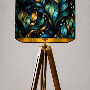 May include: A floor lamp with a dark wood tripod base and a rectangular lampshade. The lampshade features a teal, gold, and blue floral design with pearl accents. The lamp has a gold-colored metal accent.