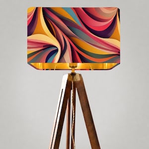May include: A floor lamp with a rectangular lampshade featuring a colorful, abstract design of swirling lines in shades of yellow, orange, pink, blue, and purple. The lampshade is set on a wooden tripod base with a gold-colored interior.