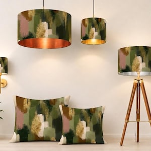 May include: A collection of home decor items featuring a matching abstract brushstroke pattern in shades of olive green, sage, brown, dusty pink, and gold. The set includes two drum pendant lights, a wall sconce, a tripod floor lamp, and two cushions.