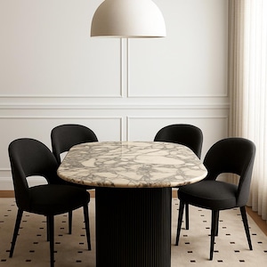 Puede incluir: Un moderno juego de comedor con una mesa redonda con tapa efecto m&aacute;rmol y una base de pedestal negra acanalada. Cuatro sillas negras tapizadas rodean la mesa. Una gran l&aacute;mpara colgante blanca en forma de c&uacute;pula cuelga encima.