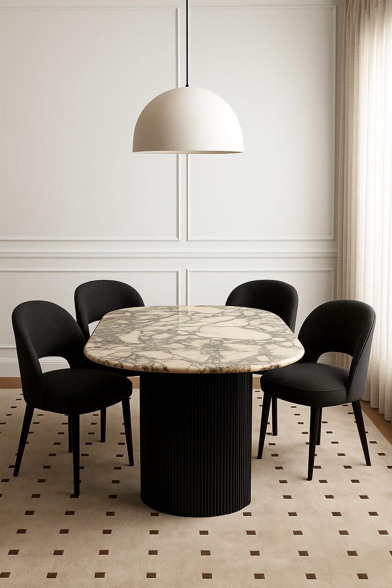 Puede incluir: Un moderno juego de comedor con una mesa redonda con tapa efecto m&aacute;rmol y una base de pedestal negra acanalada. Cuatro sillas negras tapizadas rodean la mesa. Una gran l&aacute;mpara colgante blanca en forma de c&uacute;pula cuelga encima.
