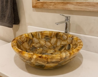 Könnte beinhalten: Ein dekoratives, rundes Badezimmerwaschbecken aus Naturstein. Das Waschbecken hat ein Mosaikmuster aus beige-, braunen und hellbraunen Teilen. Über dem Waschbecken ist ein verchromter Wasserhahn installiert. Das Waschbecken steht auf einer weißen Arbeitsplatte.