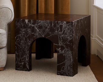 May include: A dark brown marble-look side table with a square top and arched openings. The table has a veined pattern in shades of white and gray. The table is a modern accent piece.