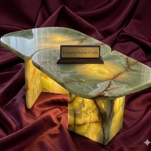 May include: A distinctive, two-part onyx table with a green and brown marbled surface. The table emits a warm, yellow glow. The text "Elegance Indian Crafts" is displayed on a small, rectangular plaque.